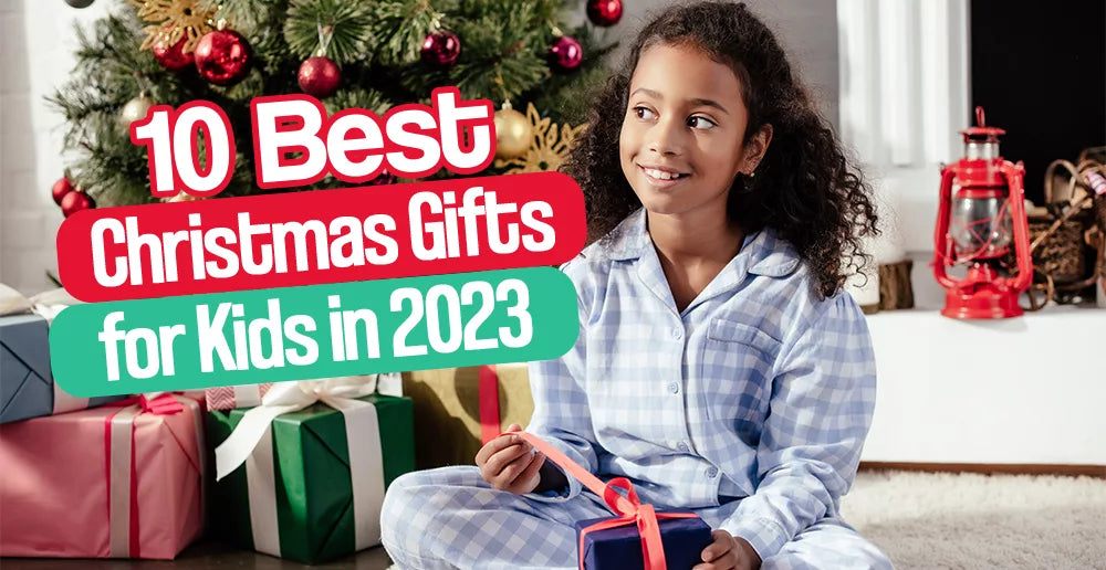 smiling girl in pajamas holding a Christmas gift with decorated tree and wrapped presents in the background titled 10 Best Christmas Gifts for Kids in 2023
