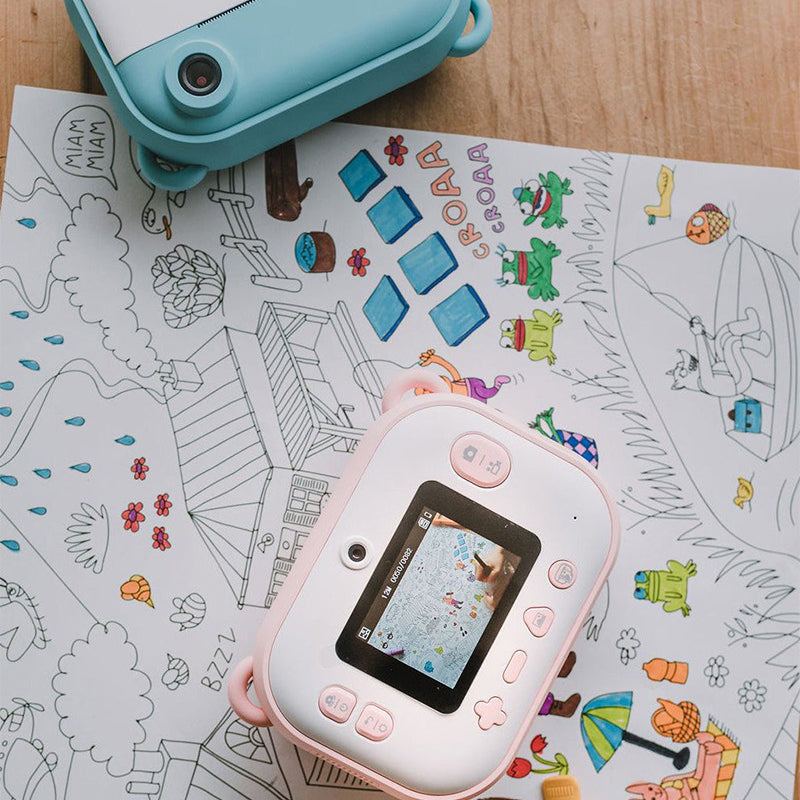 Kid Instant Print Camera in pink on a coloring sheet with a blue camera partially visible on a wooden surface