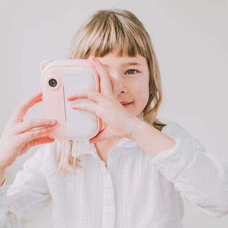 Child holding a pink Kid Instant Print Camera capturing a photo in a white background