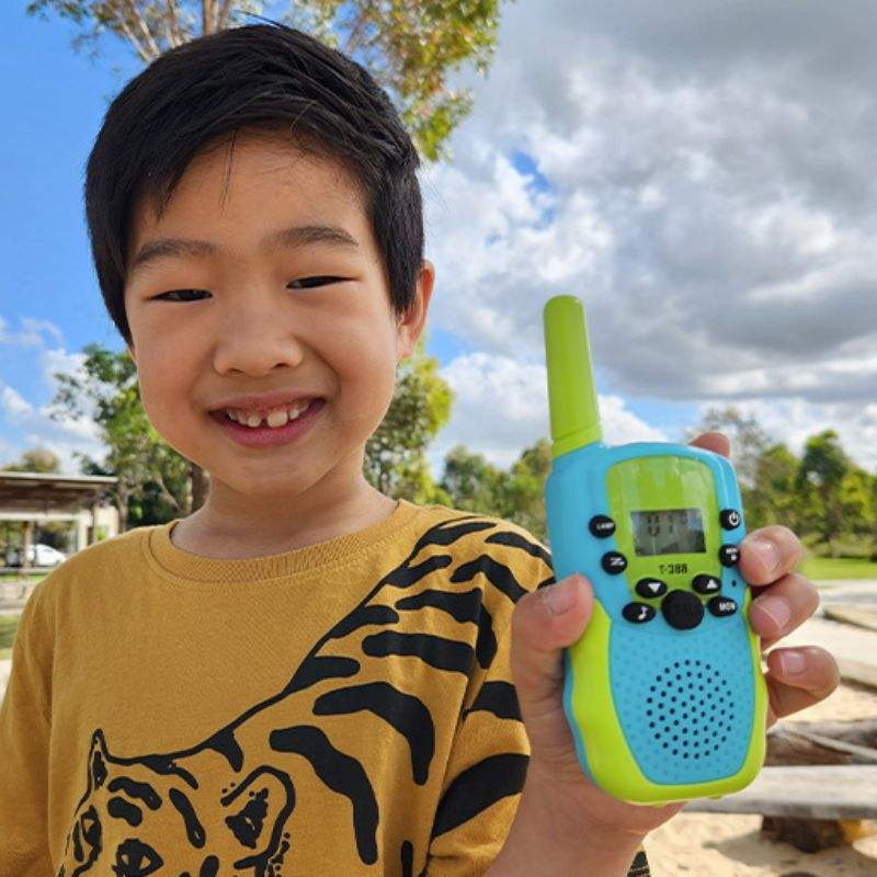 Child holding a blue and green kids walkie talkie outdoors on a sunny day